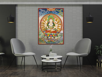 Hand-painted Chundi thangka on a grey brick wall between two chairs: the white many-armed goddess in a circle of light