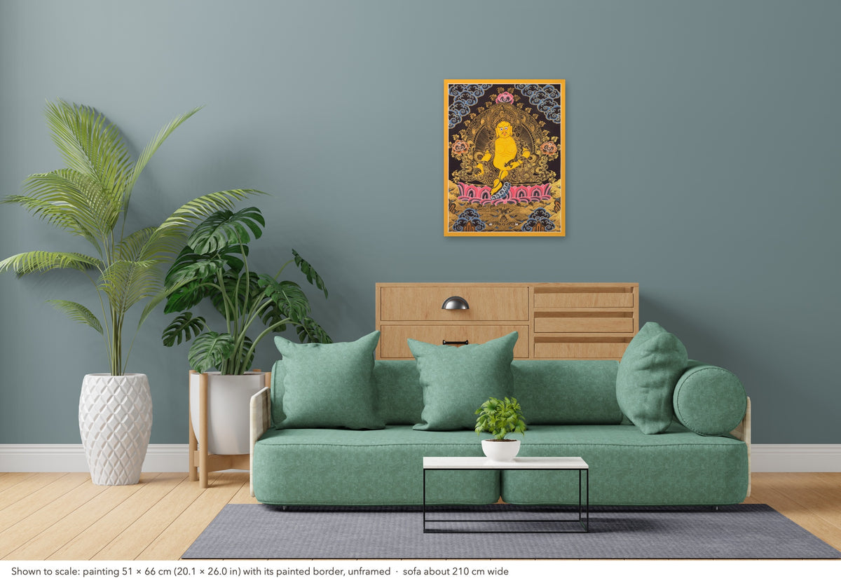 Yellow Jambhala thangka shown to scale in a living room, unframed, above a sofa about 210 cm wide (51×66 cm)