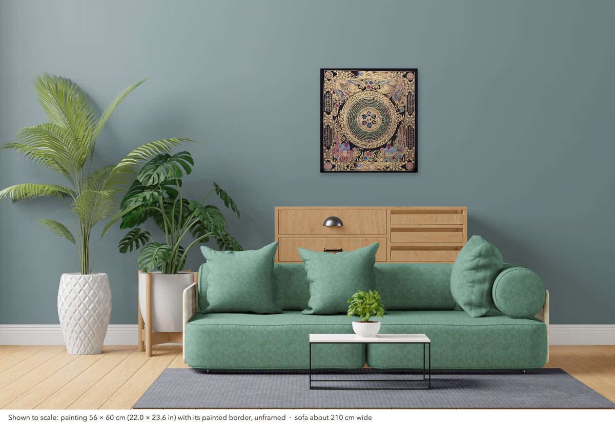 Mantra Mandala thangka shown to scale in a living room, unframed, above a sofa about 210 cm wide (56×60 cm)